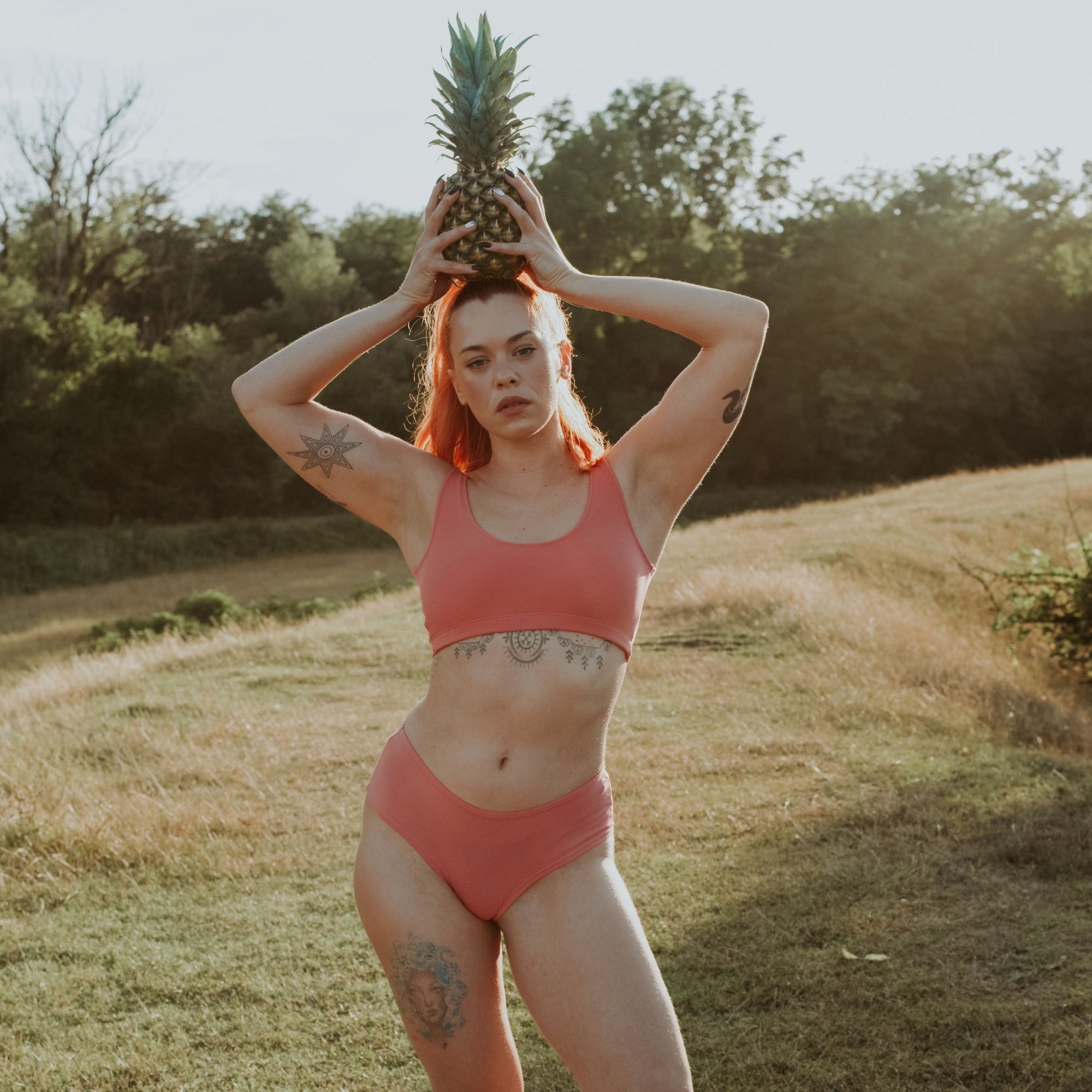 Woman wearing Desert Rose Organic Cotton Hipster Panty Hipster Panty holding pineapple on her head in a sunlit outdoor setting.