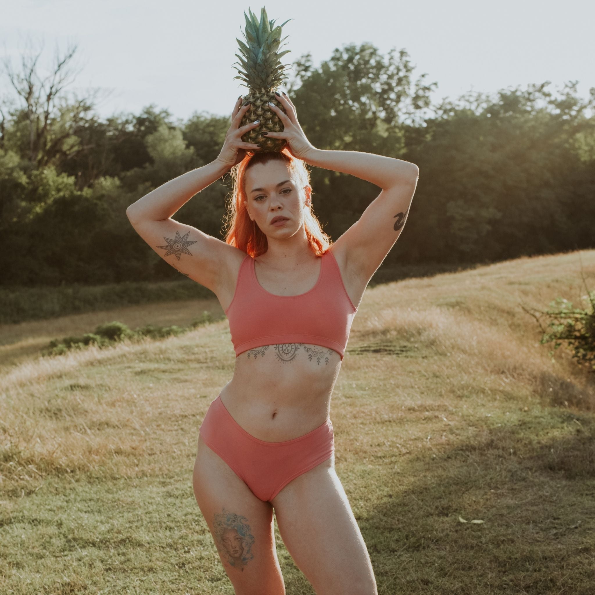 Woman wearing Desert Rose Organic Cotton Hipster Panty Hipster Panty holding pineapple on her head in a sunlit outdoor setting.
